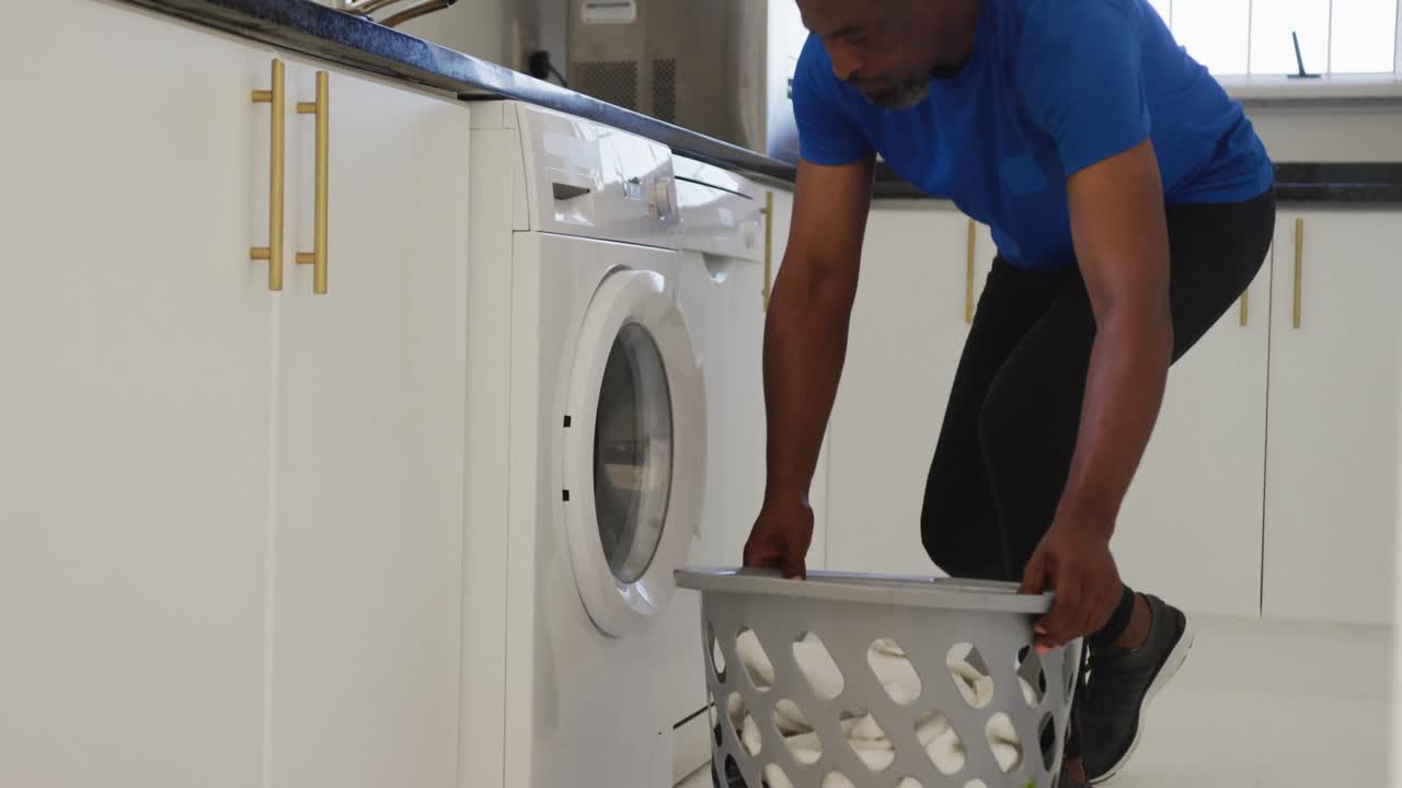 hombre mayor afroamericano poniendo la ropa sucia en la lavadora en casa