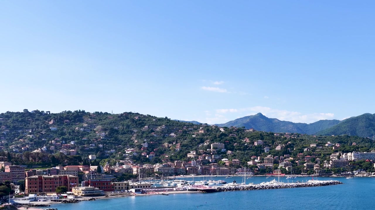 Inquadratura ampia statica di un pittoresco villaggio costiero mediterraneo e del suo porto in una giornata di sole.