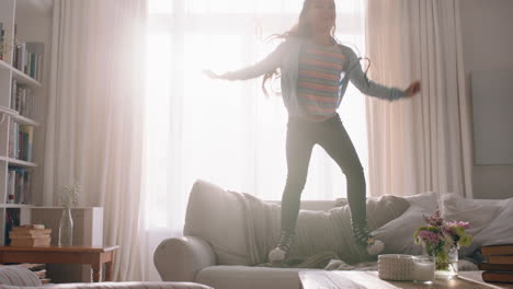 happy little girl jumping on sofa dancing having fun child in playful mood enjoying weekend morning at home with sunlight shining through window 4k footage