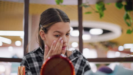 la chica aplica cuidadosamente el maquillaje mientras se mira en el espejo, asegurando una cobertura suave y uniforme, se centra en los detalles faciales, ajustando su maquillaje con precisión para un aspecto impecable y radiante
