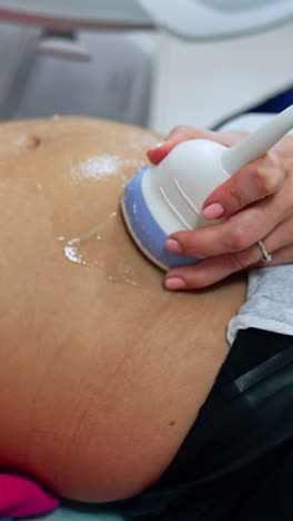 pregnant belly of a woman on the early stages of pregnancy. doctor's hand uses device to check the baby on the ultrasound machine. vertical video