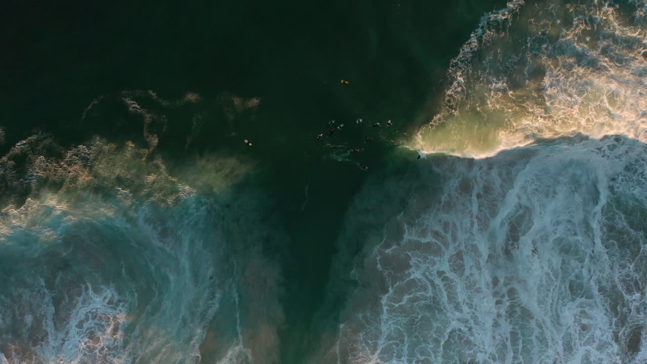 Bird's eye view of a group surfers in beautiful green aqua water during sunset while cathing waves in Cape Town, South Africa
