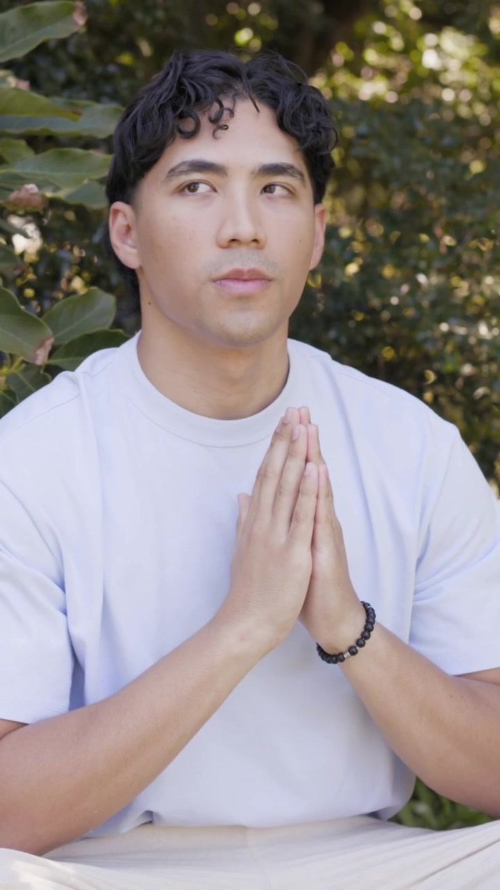 Vertical video: Sitting man holding palms on low bench, opening eyes after exhale for meditation