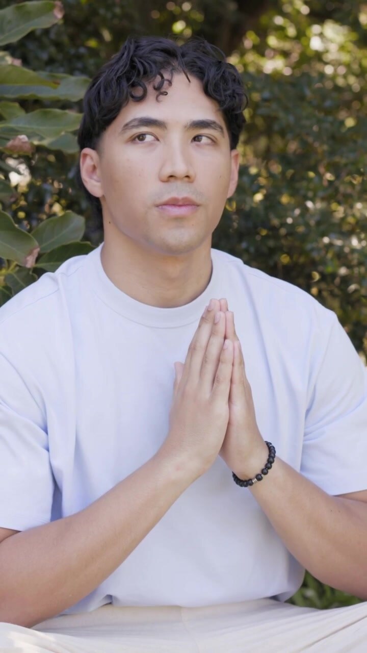 Vertical video: Sitting man holding palms on low bench, opening eyes after exhale for meditation