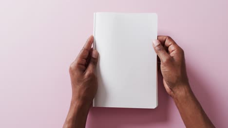 cerca de las manos sosteniendo un libro con página negra espacio de copia en fondo rosa en cámara lenta