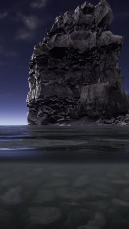rock formation rising from calm ocean waters at dusk during twilight hours
