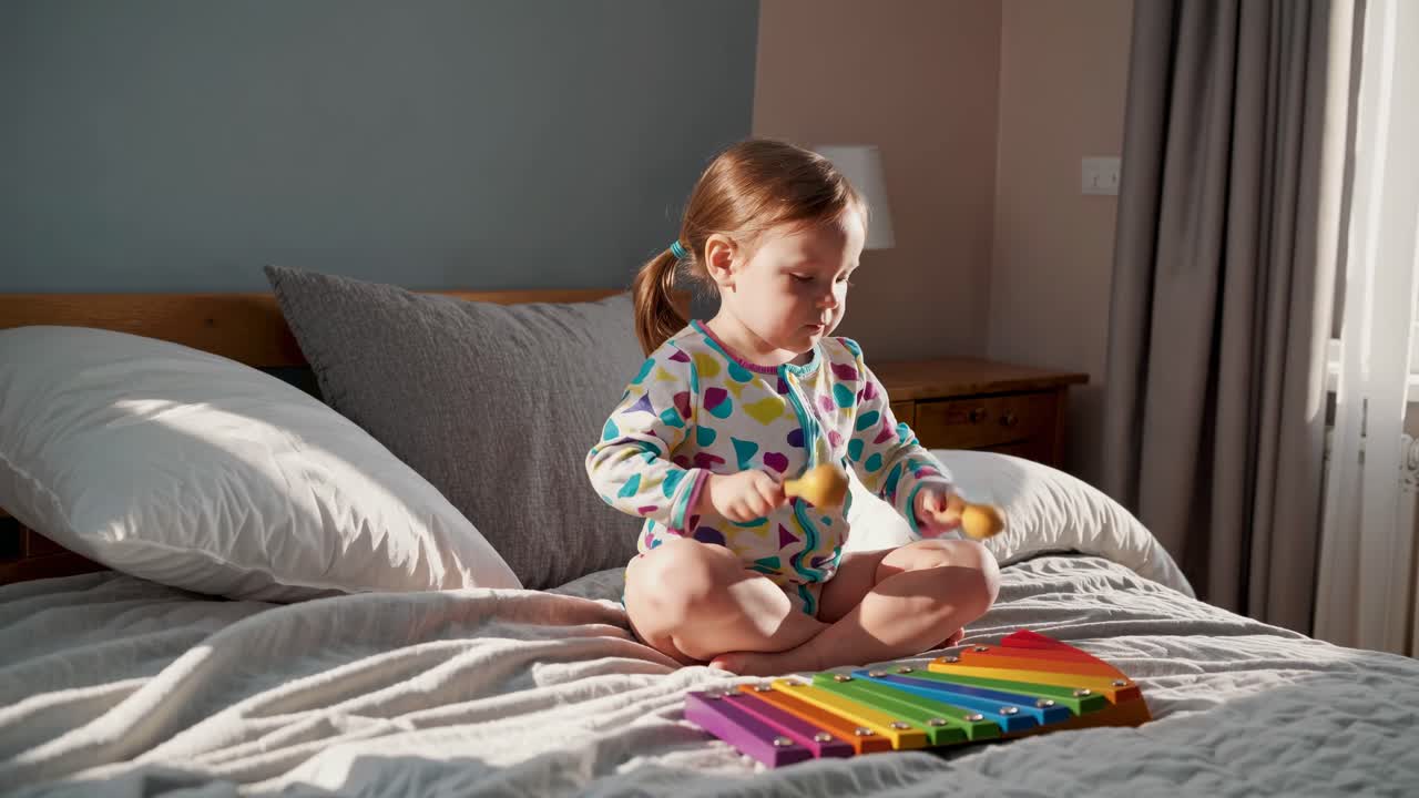Toddler Playing Musical Instruments on a Bed