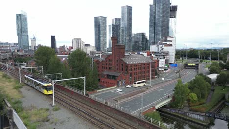 Luftdrohnenflug-über-Eine-Fahrende-Straßenbahn-Und-Die-Schornsteindächer-Der-Castlefield-Quays,-Um-Langsam-Die-Wolkenkratzer-Im-Stadtzentrum-Von-Manchester-Freizulegen