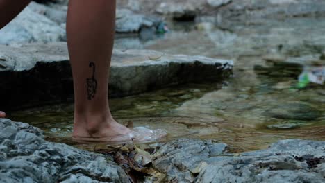 un primerísimo plano de los pies de una mujer cruzando descalzos un arroyo a cámara lenta