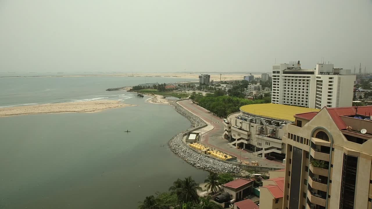 Vista aerea del lungomare di Victoria Island a Lagos, Nigeria, che mostra hotel di lusso e una costa bonificata lungo il bordo della Laguna Atlantica con acqua calma e uno skyline velato