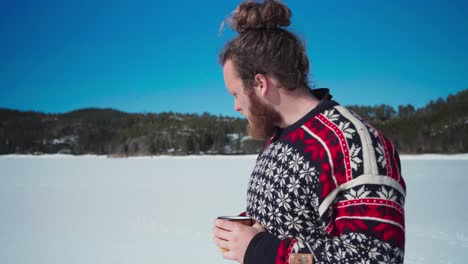 young bearded man drinking coffee with snowy landscape and blue sky in the background