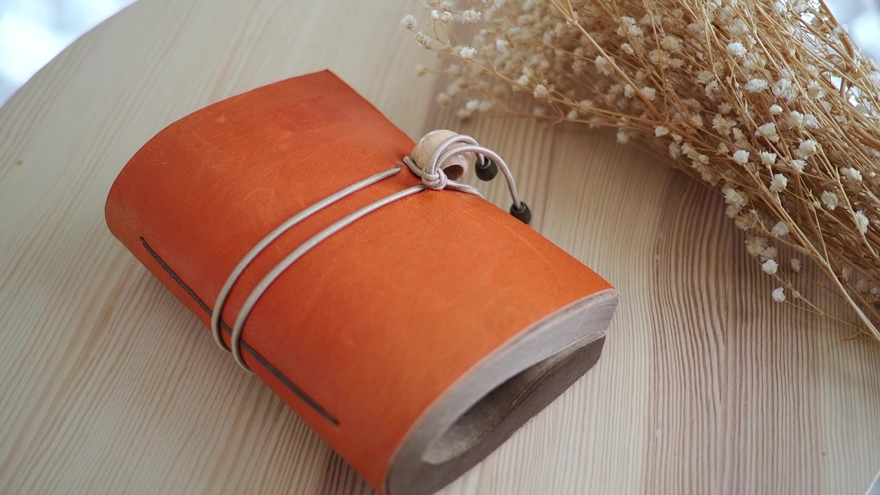 Orange Leather Journal with Dried Flowers on Wooden Table