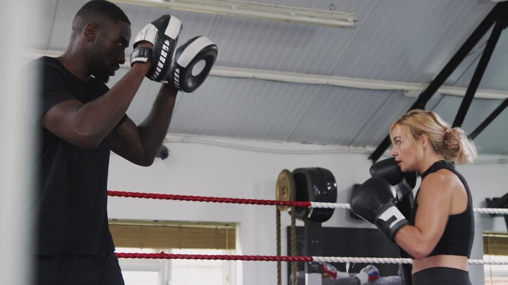 Allenatore di boxe maschio con pugile donna in palestra che usano guantoni da allenamento per fare sparring sul ring.