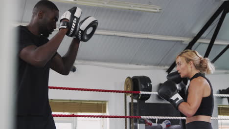 male boxing coach with female boxer in gym using training gloves sparring in ring