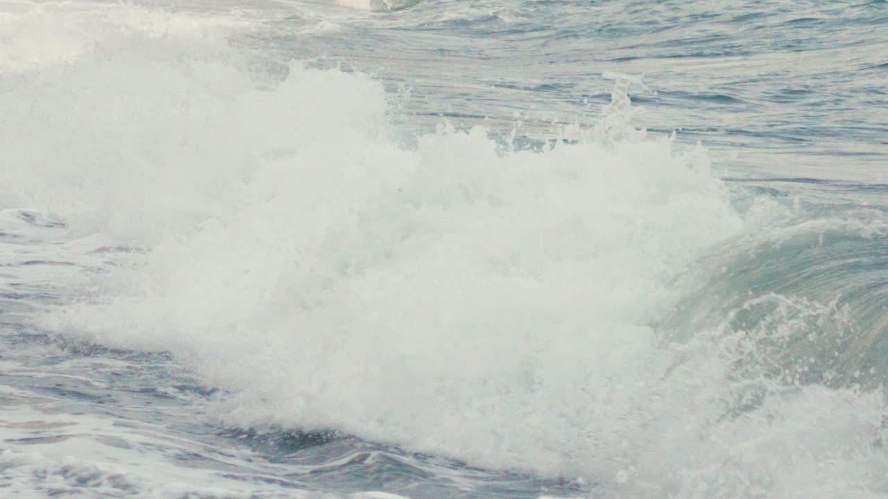 Slow motion shot of a glassy ocean wave beginning to break. Cool blue-green tones and soft surface texture create a calm, minimal visual flow