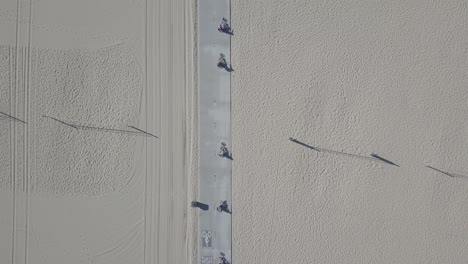 Aerial-Drone-Shot-of-5-People-on-Bikes-Riding-on-Beach-Boardwalk