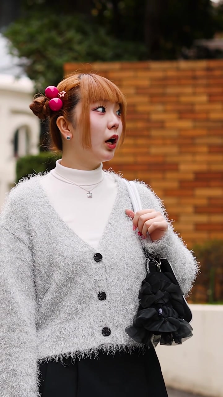 Mezza figura di donna elegante con cardigan grigio che cammina e si guarda intorno a Tokyo