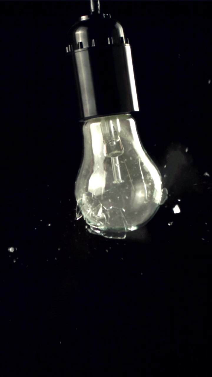 Bombilla transparente estallando en cámara lenta sobre fondo negro