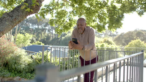 happy senior biracial man using smartphone at balcony at home, slow motion