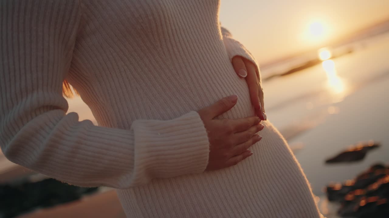 Close up of pregnant woman cradling her belly in soft light during a serene sunset moment