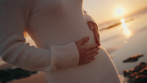 평온 한 일몰 순간 에 부드러운 빛 에 배 를 안고 있는 임신 한 여자 의 근접 사진