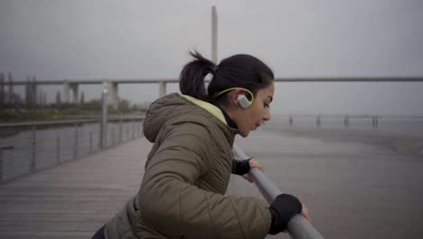 side view of cheerful hindu woman with headphones doing push ups from metal railing