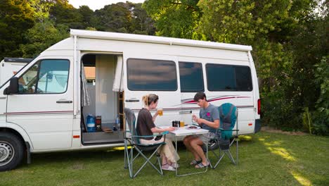 static shot of young couple eating dinner in front of their campervan in the day in new zealand