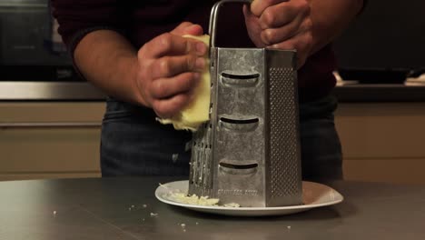a close-up of hands grating fresh cheese using a stainless steel grater in a kitchen setting. perfect for illustrating food preparation, cooking, and the use of fresh ingredients in recipes.