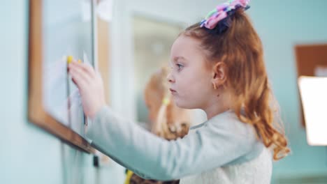 curious little girl playing with magnets on blackboard in a primary school. pretty child standing at the white board and moving colored magnets. close-up.