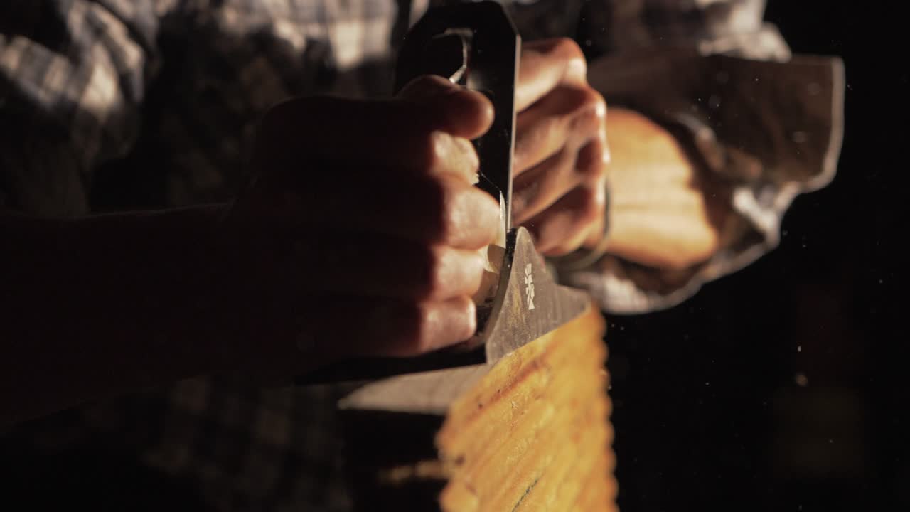 Falegname che pialla a mano legno di pino al rallentatore, con trucioli che volano via. Piano medio.