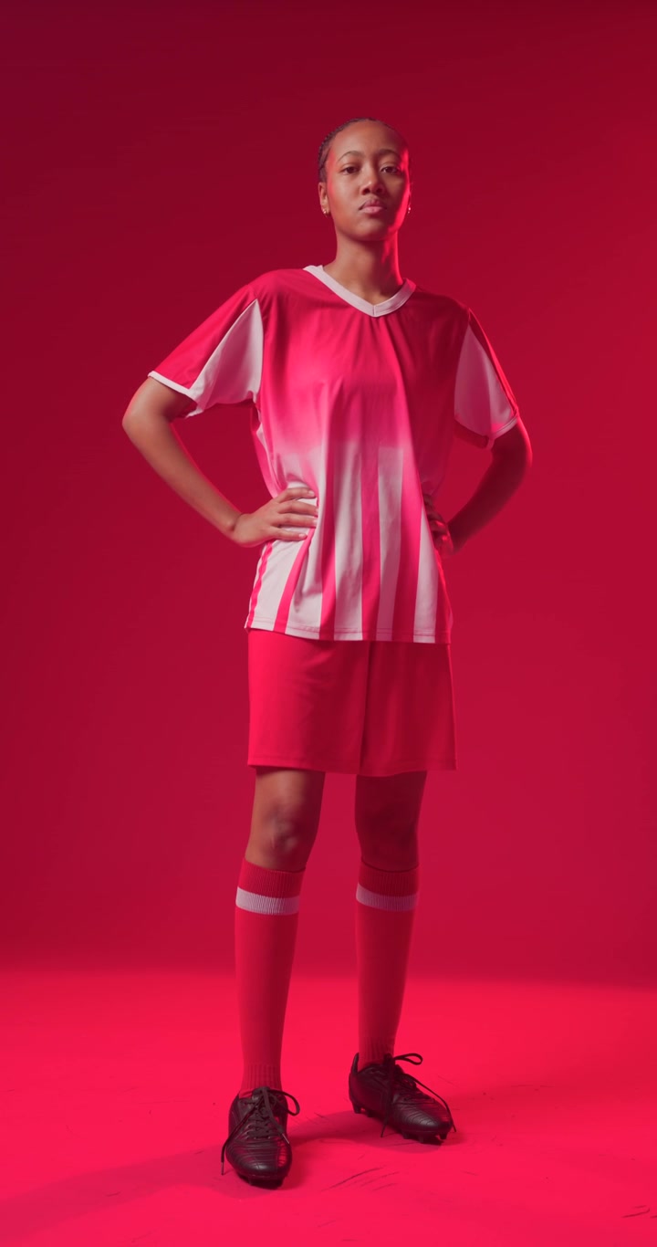Donna afroamericana che entra e si sistema la scarpa da calcio, si liscia la maglia, preparandosi a posare in un completo rosso.