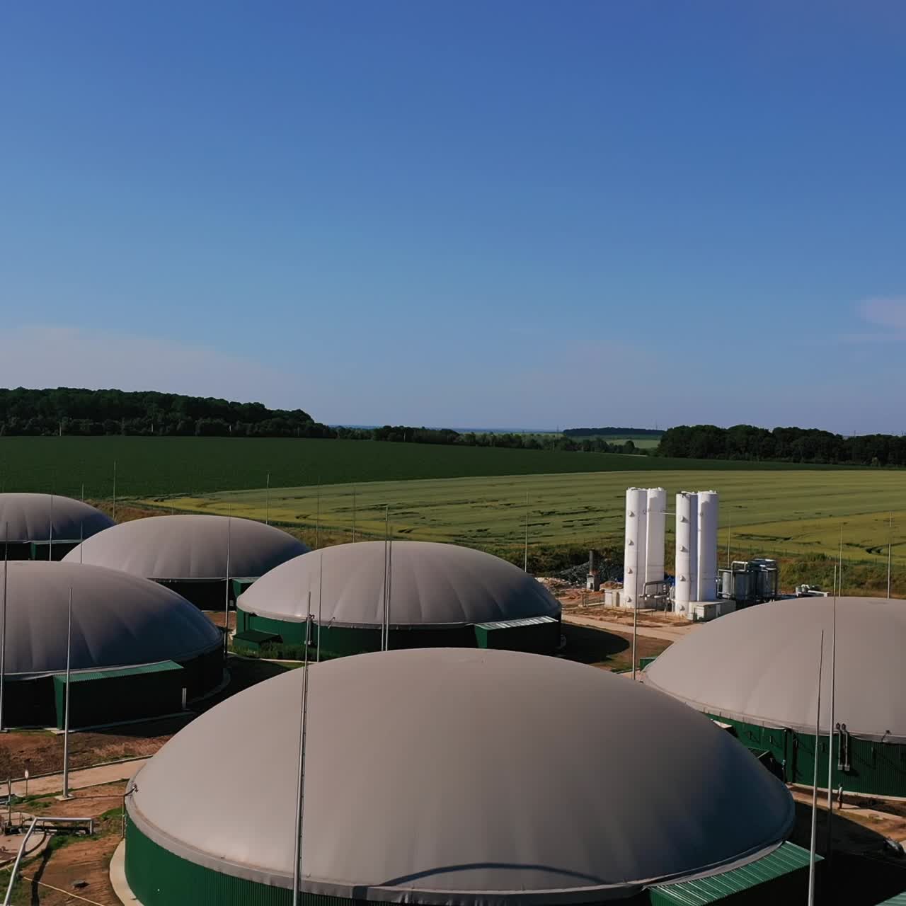 Modern biogas production plant. Round storage tanks for energy production. Green fields, forests and blue sky at the backdrop