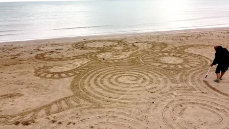 aerial view circling man creating zen sand art design on windy welsh golden beach