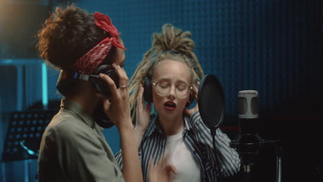 two young pretty girls singers singing in a duo and recording a new song while recording album in the sound studio