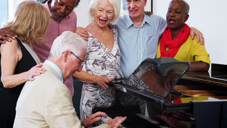 grupo de ancianos de pie junto al piano y cantando juntos