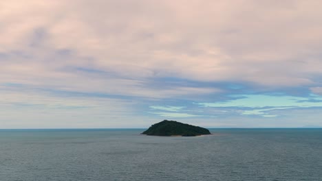 aerial footage steadily approaches a small, forested island in calm ocean waters under pastel evening clouds, with smooth forward drone movement and soft natural lighting