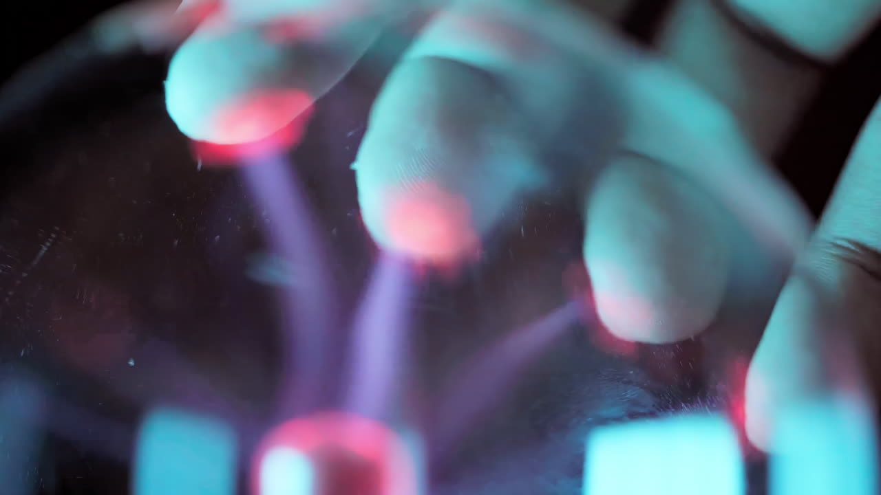 Close up finger attracting a plasma filament on a plasma ball, Hand touching with finger electric plasma ball with luminous flames in dark room