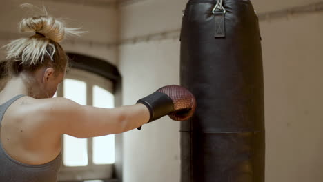 medium shot of focused woman hitting punching bag in gym