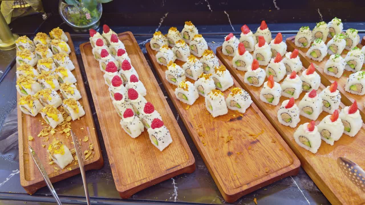 Vari tipi di involtini di sushi giapponese fresco disposti su vassoi di legno per un buffet o un evento di catering.