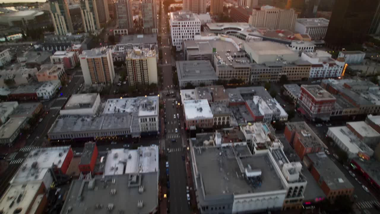 Drone voando sobre edifícios do centro de San Diego com a câmera inclinando para cima para revelar o porto e o horizonte do pôr do sol