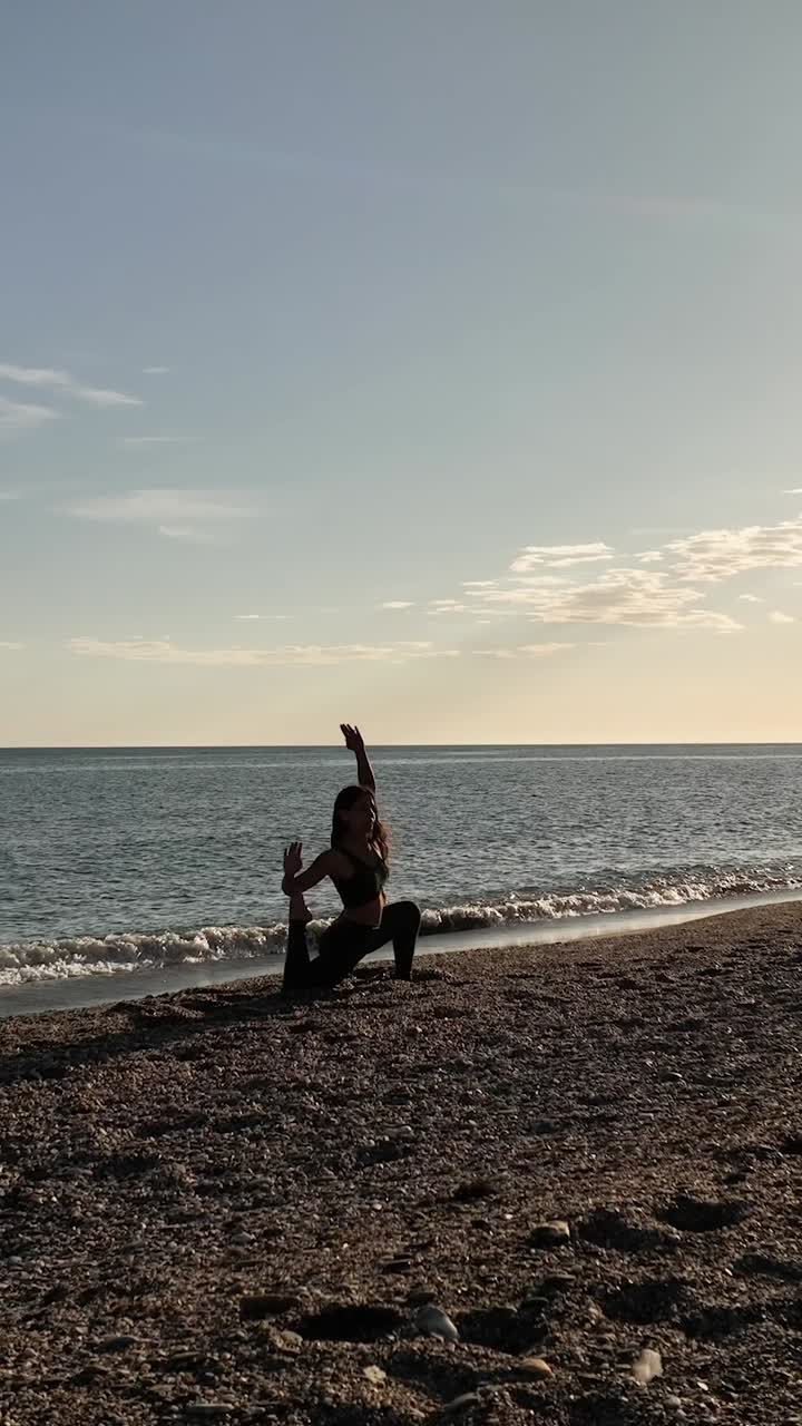 Fit female yogi stretching on sandy beach near wave