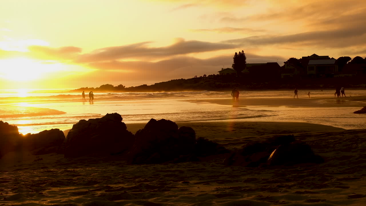 pessoas no pôr do sol passeiam na areia molhada da praia, céu dourado e oceano