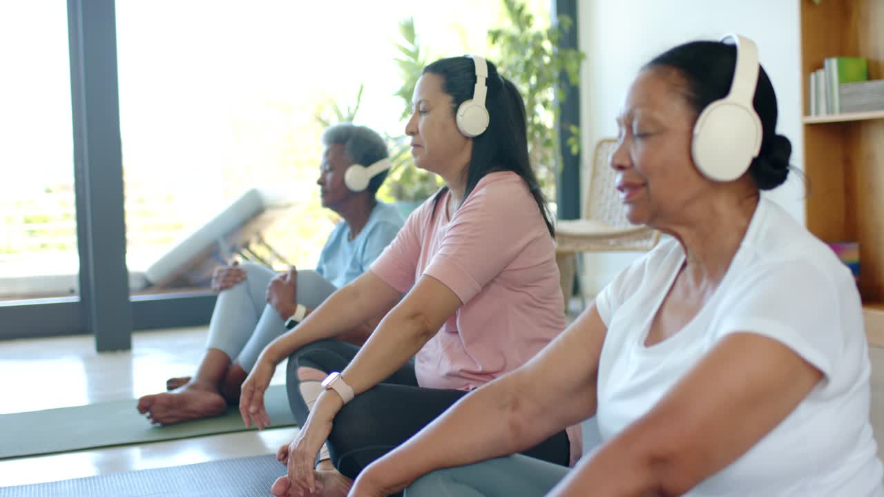 Donne afroamericane sedute su tappetini, che ascoltano una meditazione tramite cuffie per trovare la calma, con spazio per il testo.