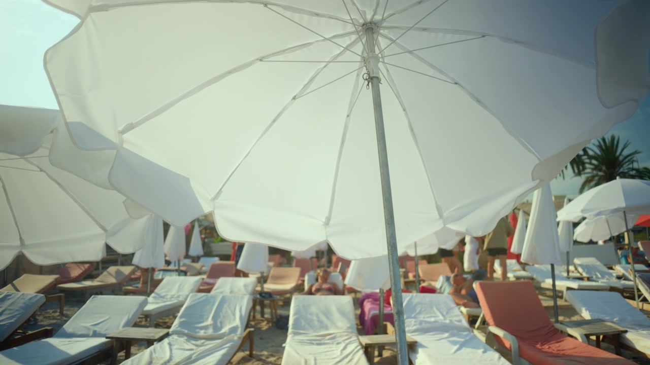 Lettini disposti su una spiaggia sabbiosa sotto una serie di ombrelloni bianchi, che offrono ombra e relax in una soleggiata giornata estiva.