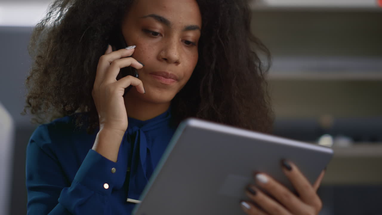 Business woman calling phone in workplace. African american worker using tablet.