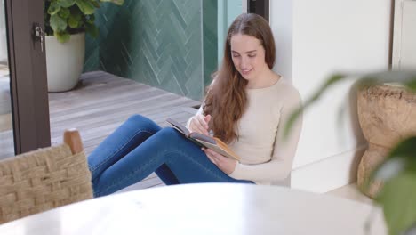 Happy-caucasian-woman-sitting-on-floor-and-reading-book-in-slow-motion