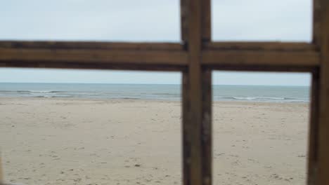 view of the baltic sea with white dunes trough the old wooden window, concept, overcast cloudy day, handheld shot