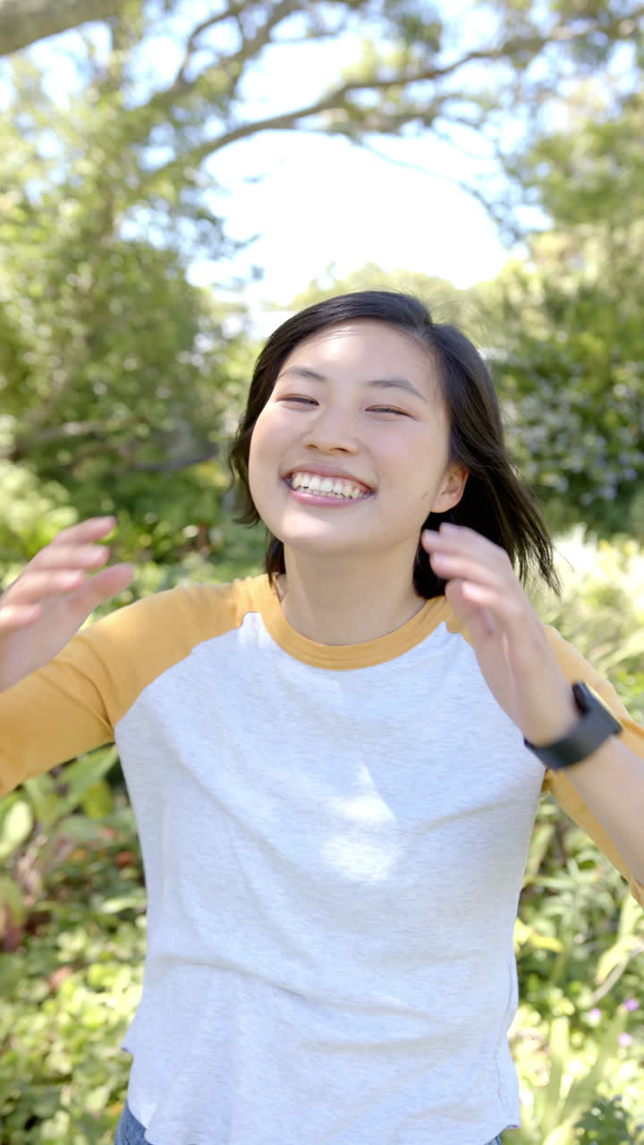 Vertical video: Smiling woman enjoying outdoor activity in sunny garden, feeling joyful and relaxed