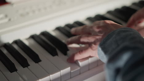 close-up shot of hands wearing a blue long sleeve playing a white piano. focus on the fingers and keys captures the movement and skill involved in performing music, with the background softly blurred