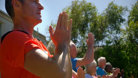 side view of caucasian male trainer training senior people in performing yoga at the garden of n 4k